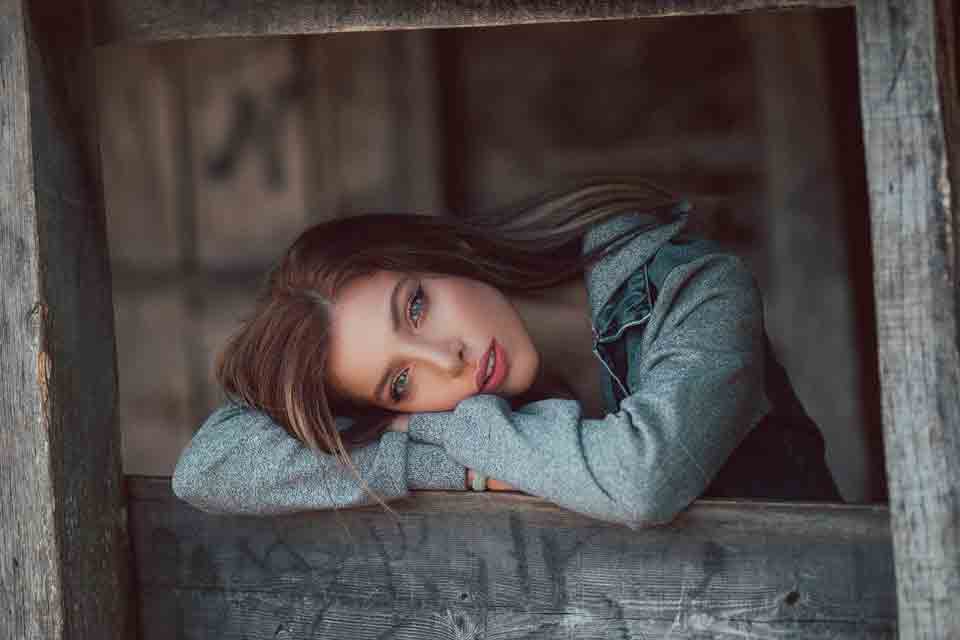 A photo of a Ukraine girl by the window resting her head on her arms.